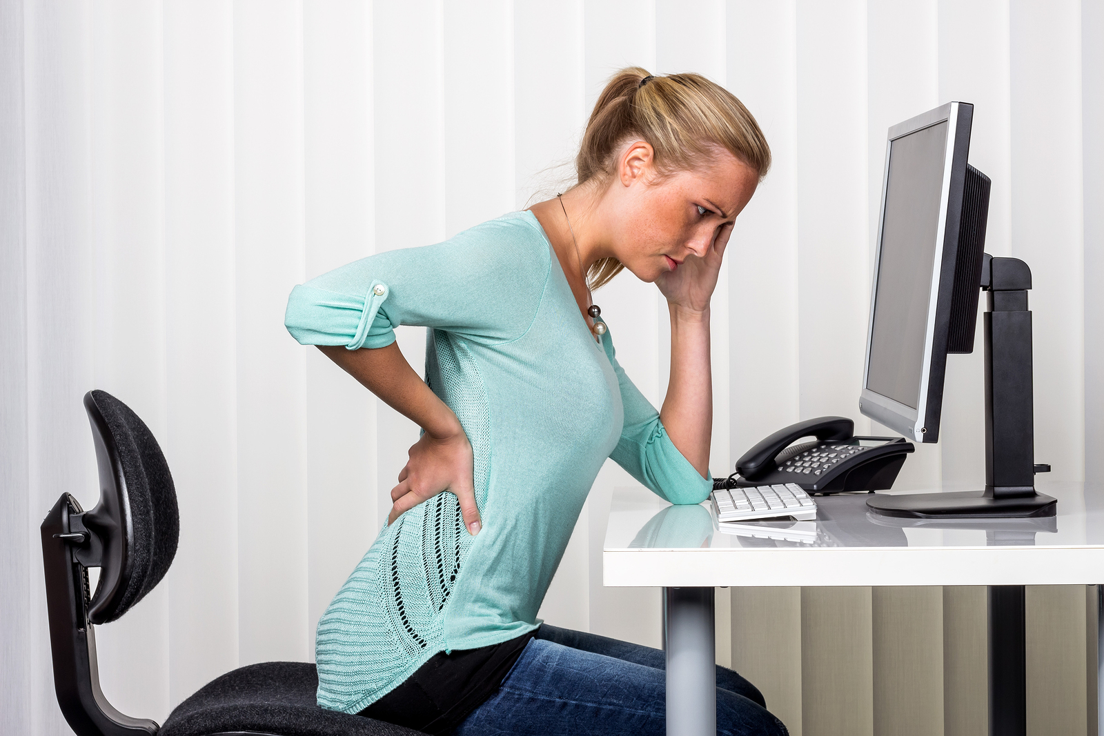 a woman sitting at a desk and has pain in the back. symbol photo